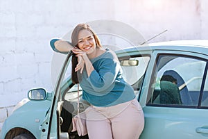 Happy plus size woman posing outside of the blue rental car in sunny day