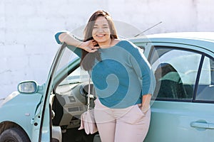 Happy plus size woman posing outside of the blue rental car in sunny day