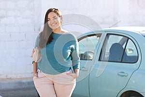 Happy plus size woman posing outside of the blue rental car in sunny day photo