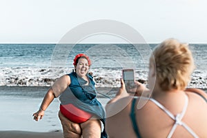 Happy plus size women having fun making photos on the beach with mobile smartphone - Overweight confident people lifestyle