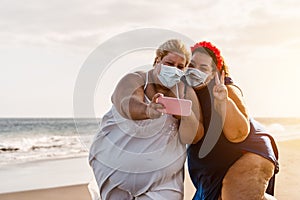 Happy plus size women taking selfie with mobile smartphone on the beach - Overweight friends having fun on vacation