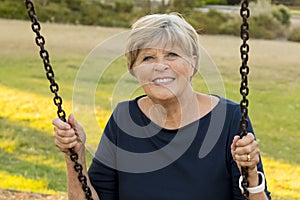Happy portrait of American senior mature beautiful woman on her 70s sitting on park swing outdoors relaxed smiling and having fun