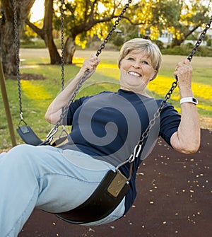 Happy portrait of American senior mature beautiful woman on her 70s sitting on park swing outdoors relaxed smiling and having fun