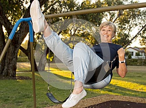 Happy portrait of American senior mature beautiful woman on her 70s sitting on park swing outdoors relaxed smiling and having fun