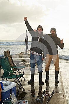 Happy, portrait and men fishing at beach with pride for tuna catch on ocean pier at sunset. Fisherman, friends and smile