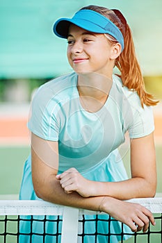 Happy portrait of a smiling teenage girl leaning on a net in a blue sportswear
