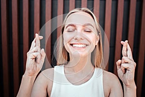 Happy and positive blonde girl is standing and keeping her eyes closed. She is smiling. Young woman is crossing her