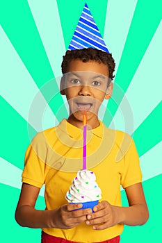 Happy, positive boy, child celebrating birthday, blowing candle on cupcake over abstract background. Contemporary art