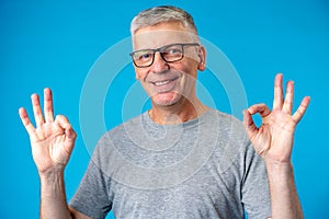 Happy positive handsome old man shows Ok sign over blue background