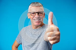 Happy positive handsome old man shows Ok sign over blue background