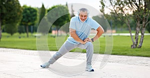 Happy positive mature sportsman in headphones doing side squat during outdoor workout