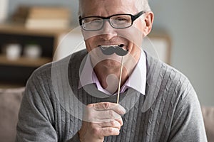 Happy positive senior man applying fake paper moustache to face