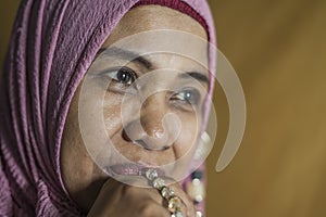 Happy and positive senior muslim woman in her 50s wearing traditional Islam hijab head scarf praying holding prayer beads in