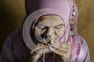Happy and positive senior muslim woman in her 50s wearing traditional Islam hijab head scarf praying holding prayer beads in