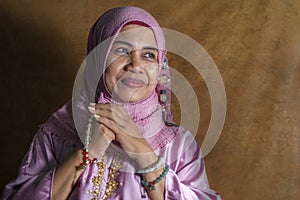 Happy and positive senior muslim woman in her 50s wearing traditional Islam hijab head scarf praying holding prayer beads in