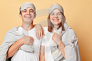 Happy positive smiling couple man and woman wrapped in blanket isolated over beige background looking at camera with happy
