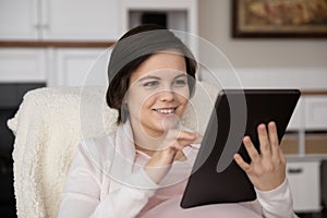 Happy positive young pregnant woman using tablet