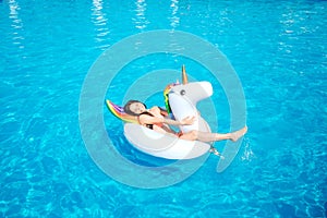 Happy and positive young woman is lying on air mattress in the middle of swimming pool. She waves with hes leg making