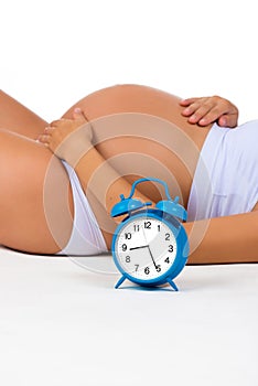 Happy pregnancy. Pregnant belly with alarm clock. Soon birth. Fetal development by months