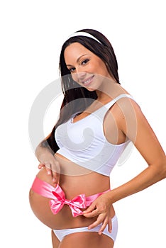 Happy pregnancy. Smiling pregnant woman tying pink ribbon bow on belly