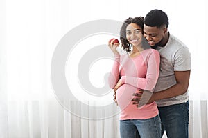 Happy pregnant african woman eating apple while husband hugging her