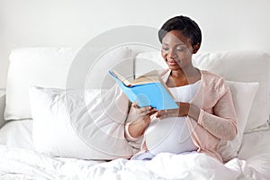 Happy pregnant african woman reading book at home