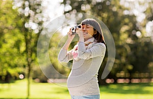 Happy pregnant asian woman with camera at park