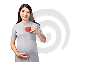 Happy pregnant asian woman holding red heart and touching her abdomen with smile face, isolated on white background and copy space