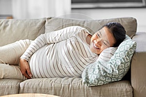 happy pregnant asian woman lying on sofa at home