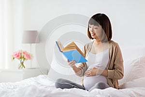 Happy pregnant asian woman reading book at home