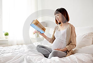 Happy pregnant asian woman reading book at home