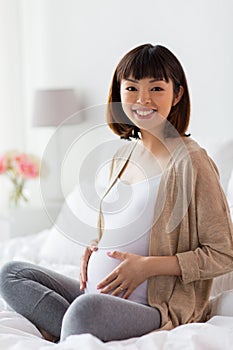 Happy pregnant asian woman sitting in bed at home