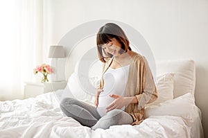 Happy pregnant asian woman sitting in bed at home