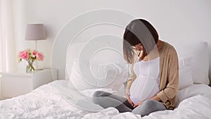 Happy pregnant asian woman sitting on bed at home