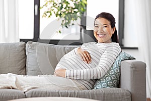 happy pregnant asian woman sitting on sofa at home