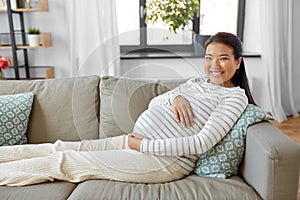 happy pregnant asian woman sitting on sofa at home