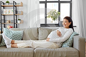 happy pregnant asian woman sitting on sofa at home