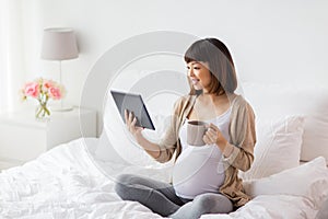 Happy pregnant asian woman with tablet pc at home