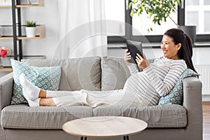 happy pregnant asian woman with tablet pc at home