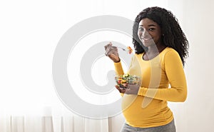 Happy pregnant black woman eating fresh salad at home