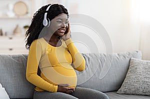 Happy pregnant black woman listening to music in headphones