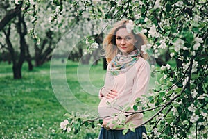 Happy pregnant blonde beautiful woman walking outdoor in spring park or garden