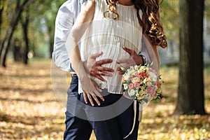 Happy pregnant bride and groom holding wedding bouquet