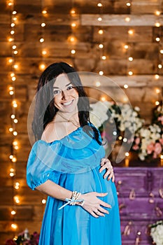 Happy pregnant brunette woman holding hands on her stomach and smiling