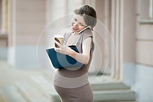 Happy pregnant business woman talking on phone and writing notes