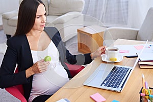 Happy pregnant businesswoman having breakfast at office