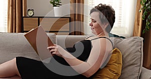 Happy pregnant caucasian woman reading book at home. Pregnant woman resting at bedroom