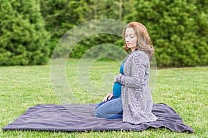 Happy pregnant caucasian woman relaxing in a park holding hands on her belly