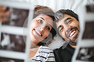 Happy pregnant couple on the bed looking at the ultrasound images of their baby