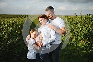 Happy pregnant couple with daughter in summer nature.